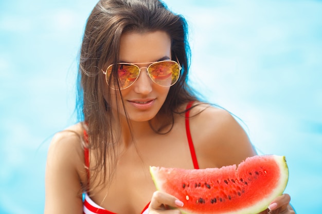 Muy bella mujer con sandía en la piscina