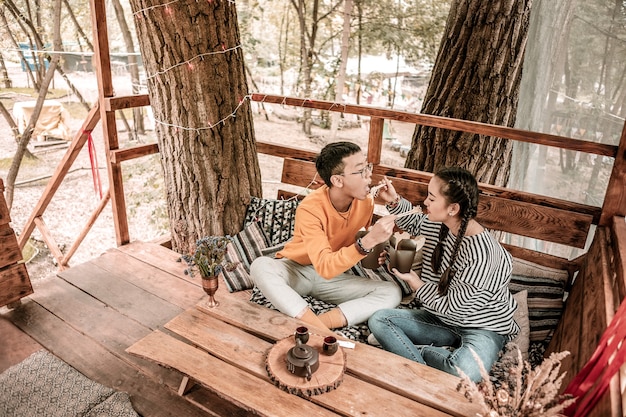 Muy delicioso. Personas juguetonas sentadas una frente a la otra mientras disfrutan de su cena al aire libre