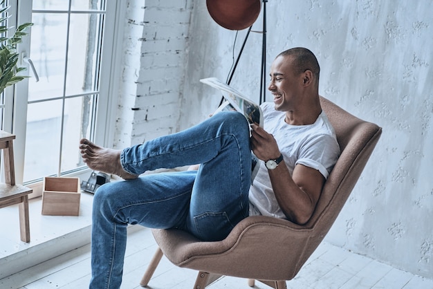 ¡Muy divertido! Vista superior del apuesto joven africano leyendo el periódico y sonriendo