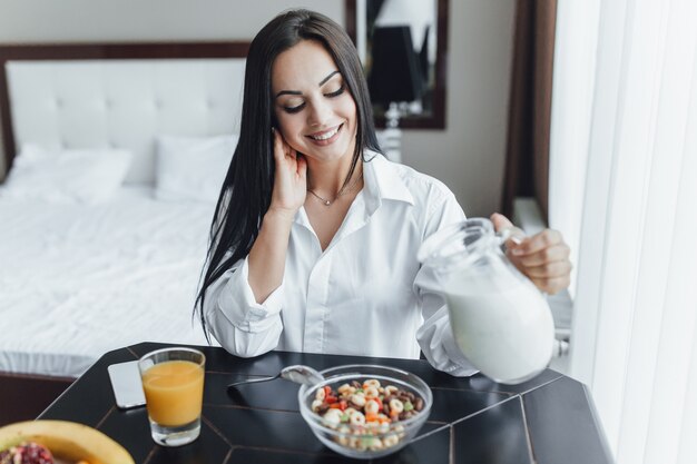 Foto muy hermosa chica morena feliz por la mañana en su habitación en la mesa de la ventana