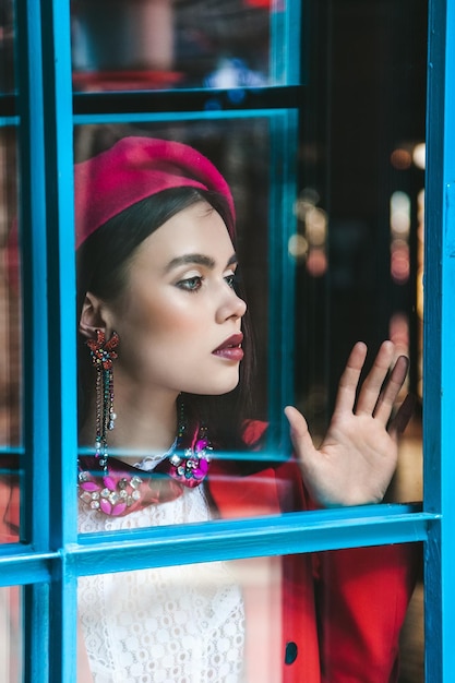 Muy hermosa modelo morena con ojos azules en una boina roja está mirando a través del cristal