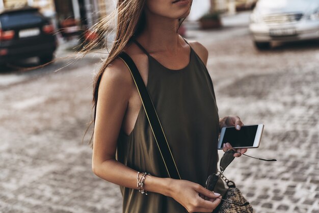 Muy ocupado al aire libre. Primer plano, de, mujer joven, tenencia, ella, teléfono inteligente, mientras, posición, aire libre