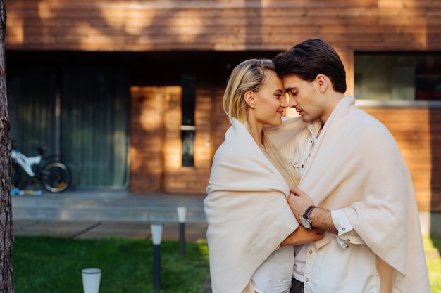 Muy romantico. Encantado de pareja alegre vistiendo un plaid mientras está de pie frente a la casa