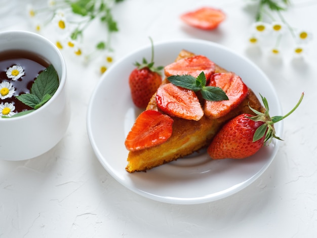 Muy sabroso pastel de zanahoria decorado con fresas en una mesa blanca y una taza de té de flores fragantes