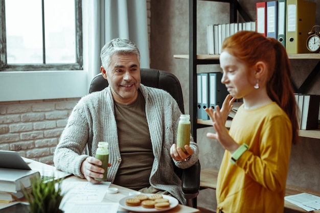 Muy saludable. Buen hombre positivo sonriendo mientras sostiene botellas con batido