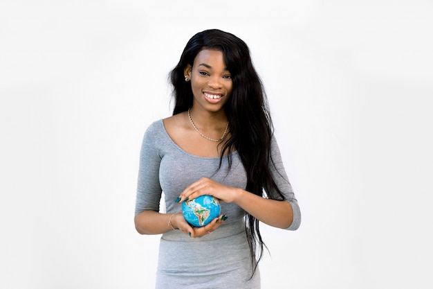 Muy sonriente joven mujer afroamericana en ropa casual sosteniendo el pequeño globo terráqueo en manos