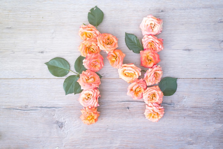 Foto n, alfabeto de flores rosas aisladas sobre fondo de madera gris, plano lay