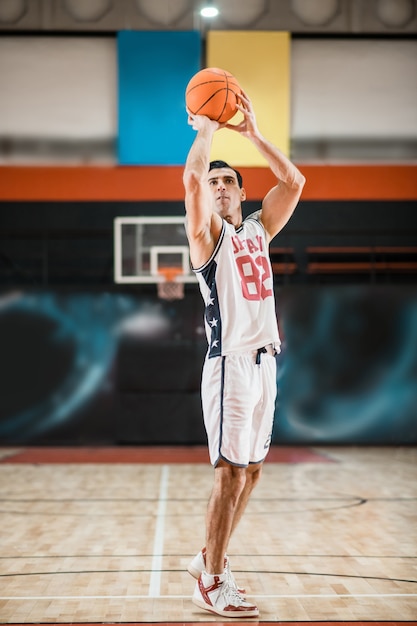 Na Academia. Jovem atlético em uma roupa esportiva branca jogando basquete no ginásio