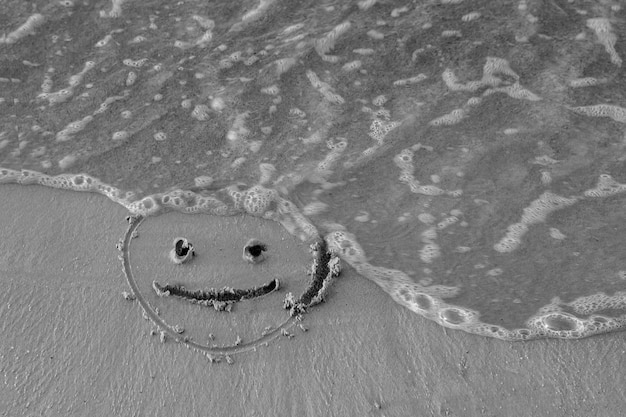 Foto na areia desenhou um rosto sorridente e uma onda lava a preto e branco