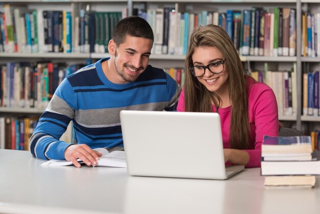 Na biblioteca bonito dois estudantes universitários com laptop e livros trabalhando em uma biblioteca da universidade do ensino médio profundidade de campo rasa