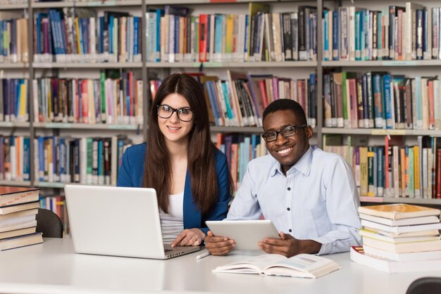 Na biblioteca Bonito dois estudantes universitários com laptop e livros trabalhando em uma biblioteca da universidade do ensino médio Profundidade de campo rasa