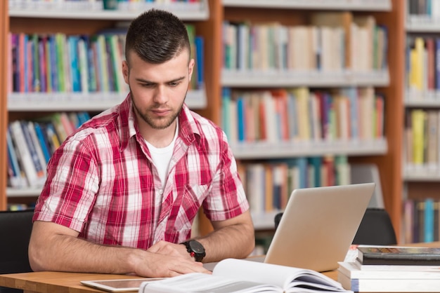 Na biblioteca Bonito estudante do sexo masculino com laptop e livros trabalhando em uma biblioteca da universidade do ensino médio Profundidade de campo rasa