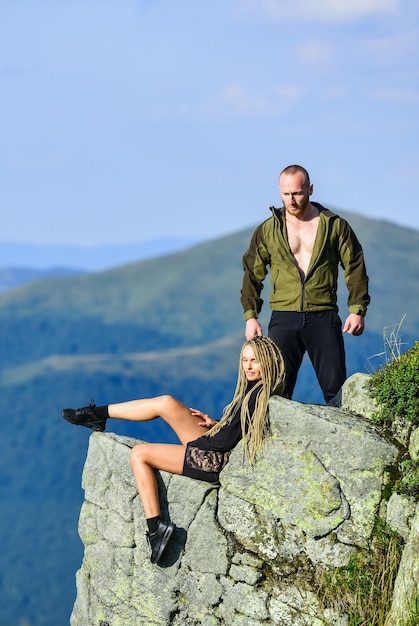 Na borda do mundo Mulher senta-se à beira do penhasco altas montanhas paisagem de fundo Caminhadas momento pacífico Caminhante turista menina e homem relaxante Casal caminhantes apreciam a vista Benefícios de caminhadas Fim de semana de caminhadas