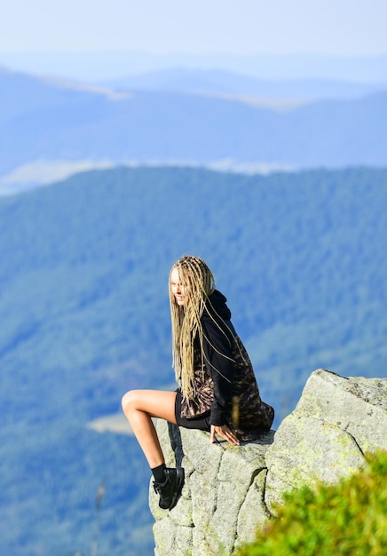 Na borda do mundo Mulher sente-se na beira do penhasco no fundo da paisagem das montanhas altas Caminhadas momento pacífico Aprecie a vista Turista alpinista garota relaxante beira do penhasco Perigoso relaxar Conceito extremo