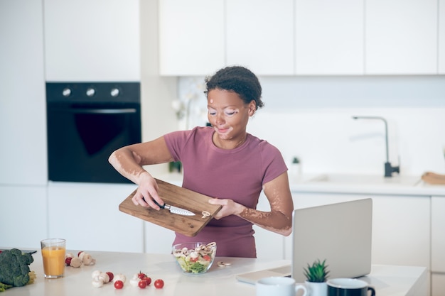 Na cozinha. uma mulher de pele escura cortando vegetais e parecendo envolvida