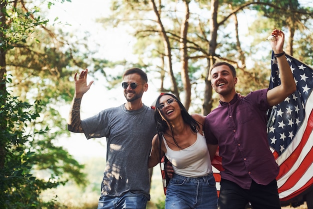 Foto na floresta. amigos têm um bom fim de semana ao ar livre perto do carro verde deles com a bandeira dos eua.