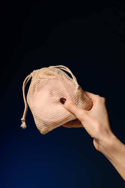Na mão, uma bolsa com uma almofada desmaquilhante rosa reutilizável de algodão em uma bolsa de tecido de malha sobre um fundo azul O conceito de ecologia e consumo consciente Discos reutilizáveis