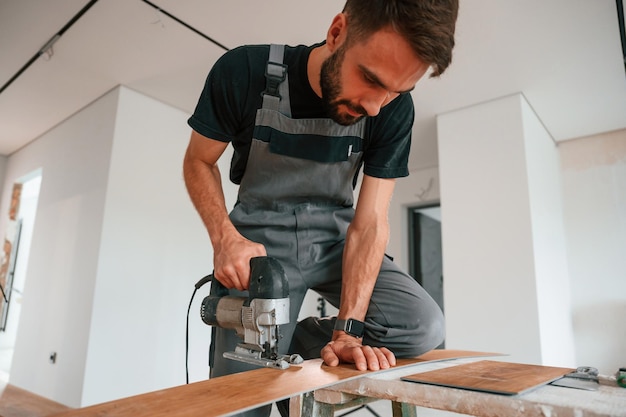 Na mesa, cortando tábuas com a broca, o homem está a instalar um novo chão de madeira laminado.