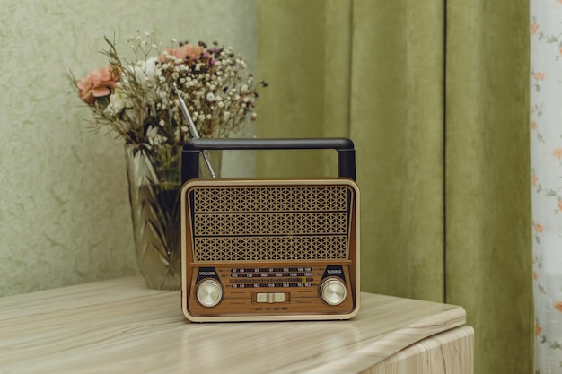 Na mesa da sala em uma mesa de madeira clara está um rádio retrô e um vaso de flores