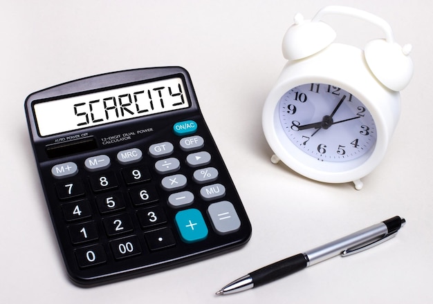 Na mesa de luz há uma calculadora preta com o texto ESCASSEZ no placar uma caneta e um despertador branco Conceito de negócio