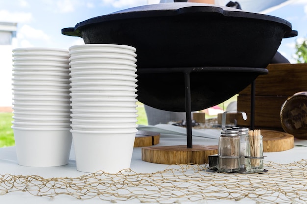 Na mesa do buffet no terraço de verão há um caldeirão de sopa de peixe A sopa é servida em tigelas de papel descartáveis Foto horizontal