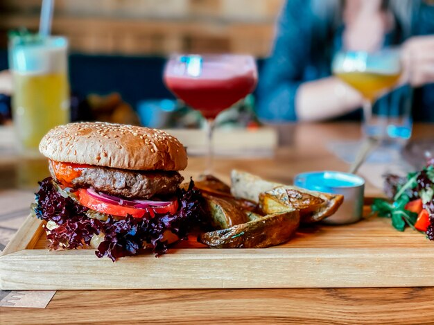 Na mesa do restaurante um hambúrguer com uma costeleta de vitela um anel de manjericão de cebola roxa um tomate e