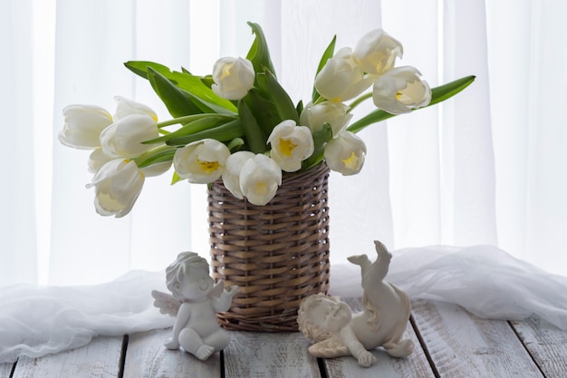 na mesa uma cesta com tulipas brancas e dois anjos brancos