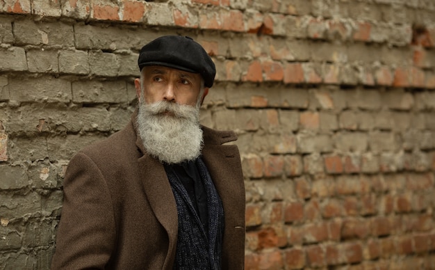 Na moda homem sênior com cabelos grisalhos e barba é ao ar livre na rua.