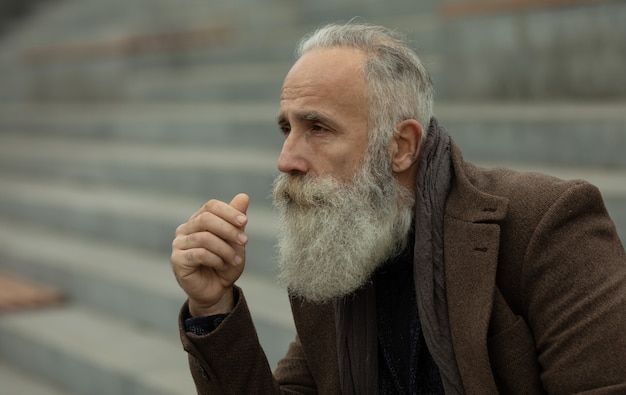 Na moda homem sênior com cabelos grisalhos e barba é ao ar livre na rua.