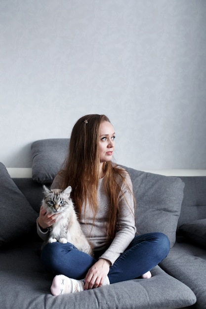 Na moda jovem sentado no sofá em casa com gato doméstico