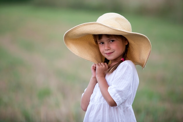 Na moda linda linda garota jovem com tranças longas no belo verão branco vestido e chapéu de palha grande.