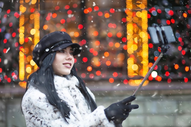 Na moda mulher morena com cabelos longos, tomando selfie em seu telefone inteligente na feira de Natal. Espaço para texto