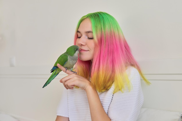 Na moda na moda com menina adolescente de cabelo tingido colorido com jovem papagaio verde quaker na mão, amizade de adolescente e pássaro, estilo de vida de adolescente e animal de estimação