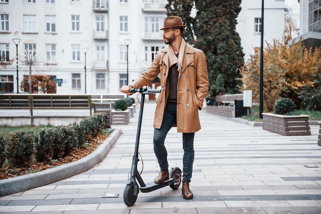 Na scooter elétrica Jovem modelo masculino em roupas da moda está ao ar livre na cidade durante o dia