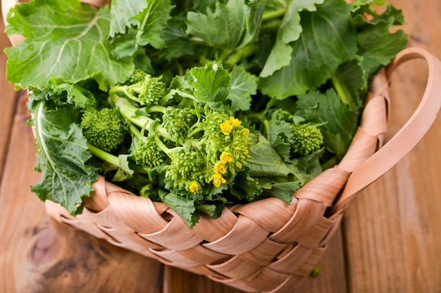 Foto nabos orgánicos crudos verdes listos para comer sobre un fondo de madera marrón. canasta con vegetales verdes frescos. comida italiana.