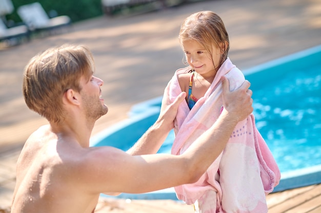 Nach dem Schwimmen. Ein junger Mann, der sein Kind mit einem Handtuch trocknet, trägt den Pool