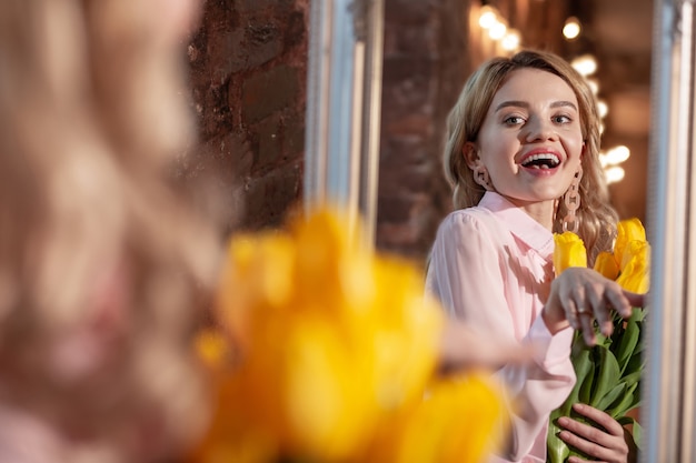 Nach einem romantischen Date. Stilvolle strahlende blonde Frau, die sich nach einem romantischen Date glücklich fühlt, während sie schöne gelbe Blumen hält holding