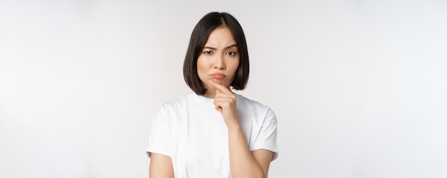 Nachdenkliche asiatische Frau, die beiseite schaut und darüber nachdenkt, Annahmen zu machen oder etwas zu wählen, das über weißem Hintergrund steht