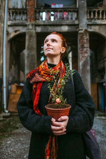 Foto nachdenkliche frau hält eine topfpflanze, während sie gegen ein gebäude steht