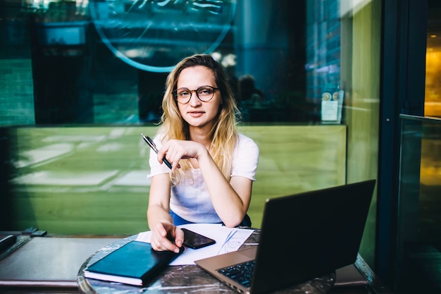 Nachdenkliche Frau mit Brille und Stift, die am Tisch arbeitet