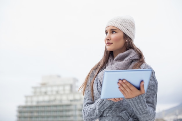 Nachdenkliche Frau mit Winter kleidet an unter Verwendung ihrer Tablette