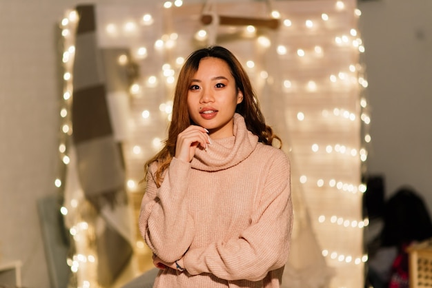 Nachdenkliche junge hübsche asiatische Frau mit brennenden Kerzen an Heiligabend, die Wünsche macht