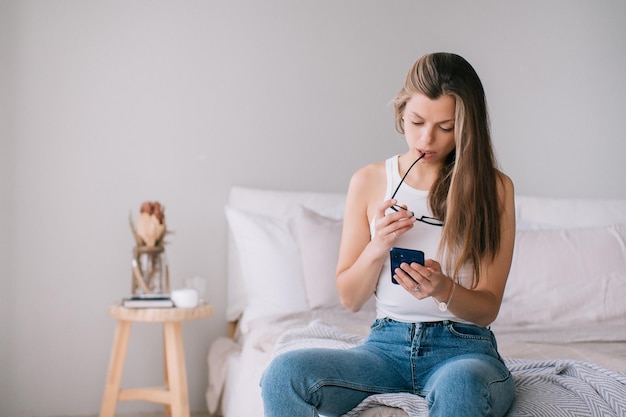 Nachdenkliche kaukasische junge erwachsene Frau in Blue Jeans und weißem T-Shirt hält Telefon liest unerwartet