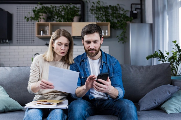 Nachdenkliche Männer und Frauen, die zu Hause Rechnungen bezahlen, nutzen die Anwendung am Telefon, um den Papierkram ernst zu nehmen