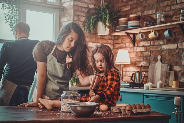 Nachdenkliche Mutter und ihre kleine Tochter kochen gemeinsam etwas in der Küche.