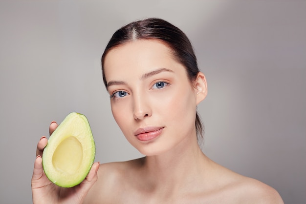 Nachdenkliche nackte Dame mit perfekter reiner Glanzhaut mit Avocado in der Hand