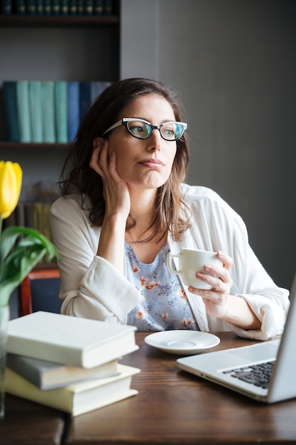 Nachdenkliche reife Frau, die Tasse Tee hält und wegschaut