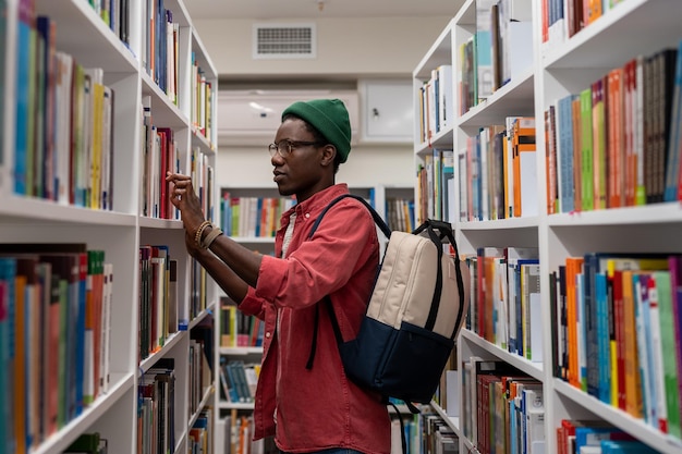 Nachdenklicher afroamerikanischer Student mit Brille wählt ein Buch in der Universitätsbibliothek oder im Buchladen aus