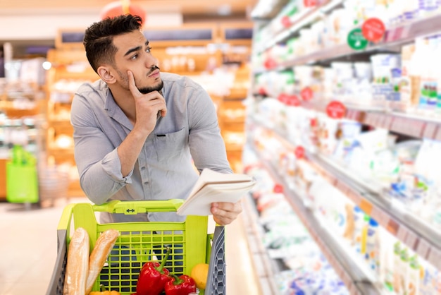 Nachdenklicher arabischer Mann, der Lebensmitteleinkäufe macht und die Preise im Supermarkt berechnet