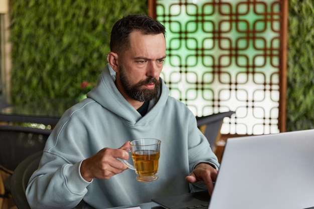 Nachdenklicher bärtiger Mann in Freizeitkleidung im Café mit Laptop